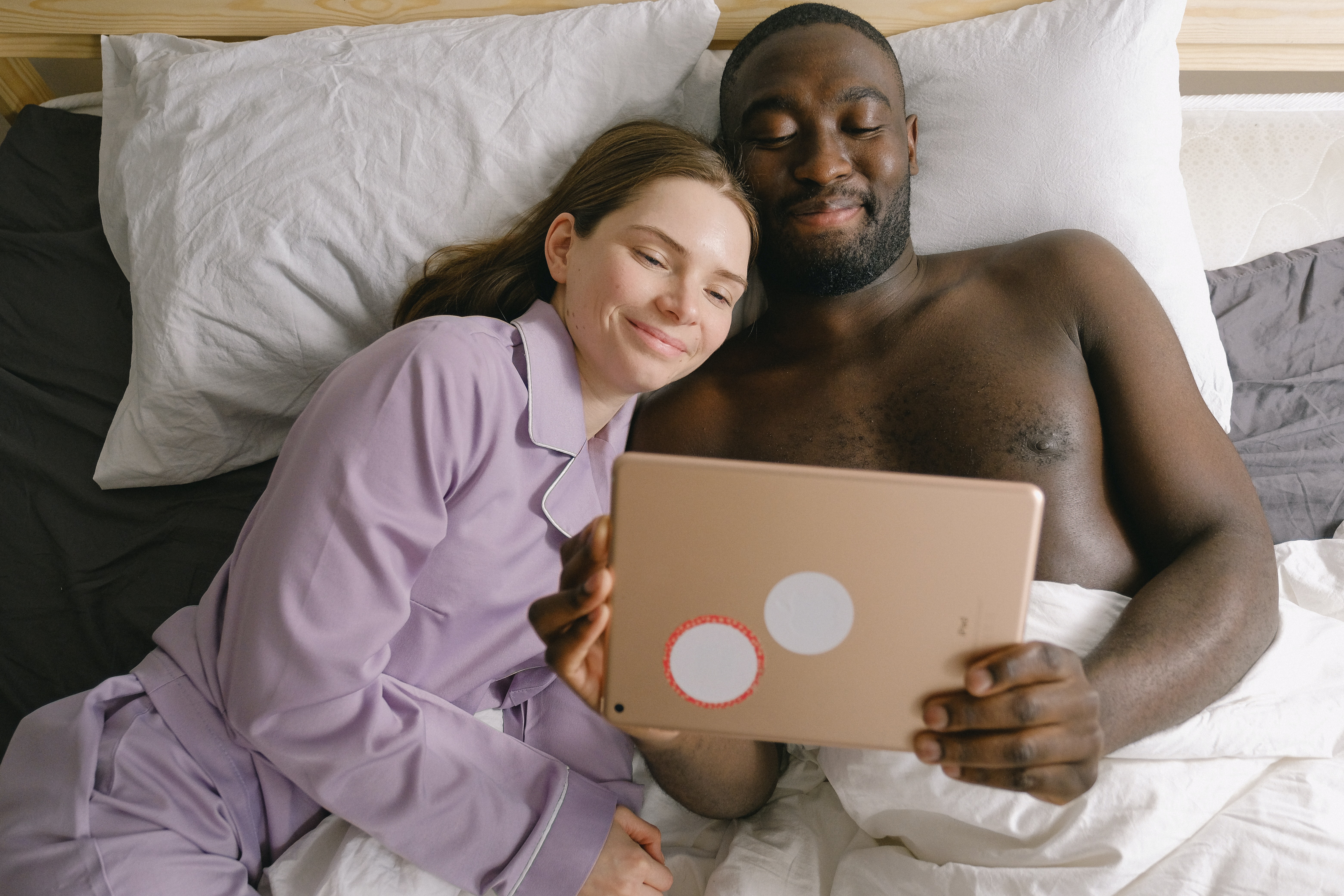 mixed race couple in bed, watching something on a tablet