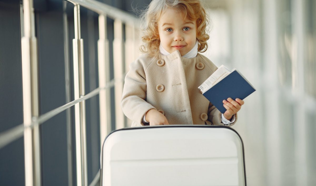 A young girl at an airport, holding a passport and with a suitcase
