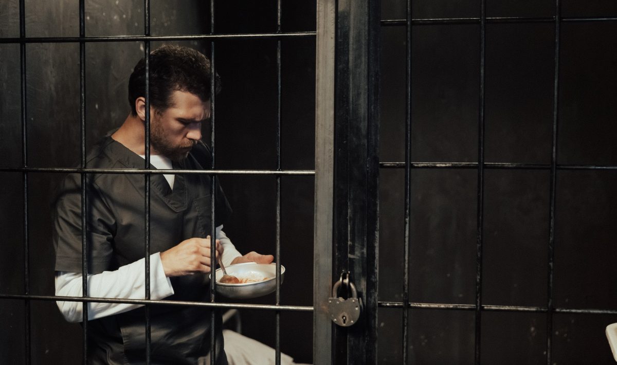 white man behind bars with bowl of food