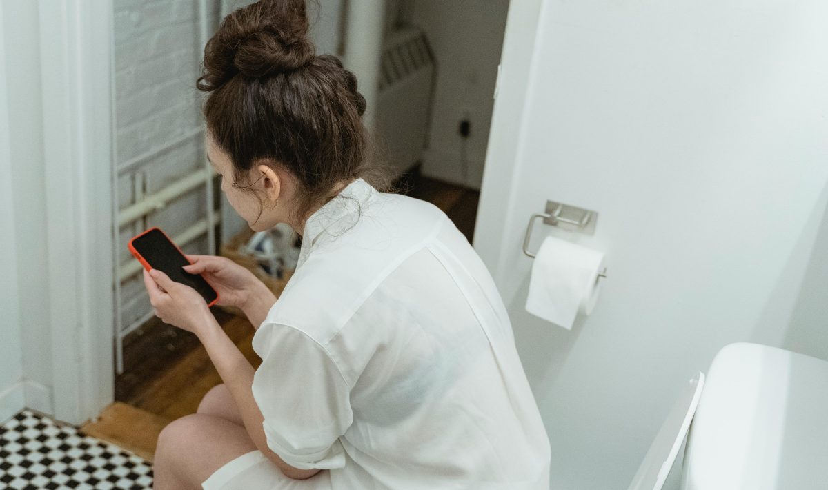 woman sitting on toilet and holding mobile phone